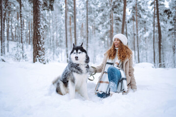 Fototapeta na wymiar Cute woman spends time with her husky dog in the winter snowy forest. Happy pet dog owner having fun together outdoors. Fun concept. Lifestyle.