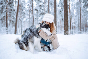 Cute woman spends time with her husky dog in the winter snowy forest. Happy pet dog owner having fun together outdoors. Fun concept. Lifestyle.