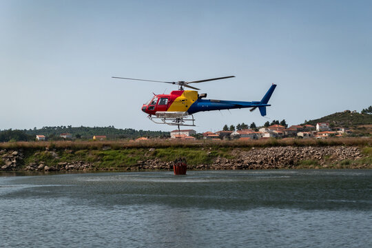 Helic&oacute;ptero bombeiro a abastecer o balde suspenso num lago para o combate a um inc&ecirc;ndio florestal