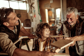 Adorable little boy working with older carpenters in workshop