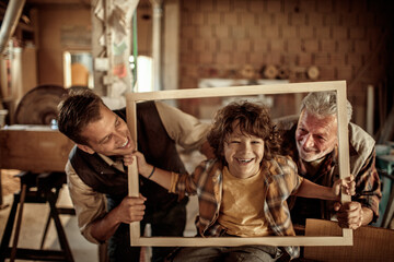 Adorable little boy working with older carpenters in workshop