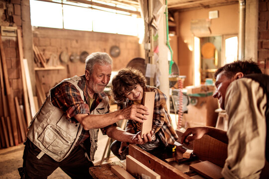 Adorable little boy working with older carpenters in workshop