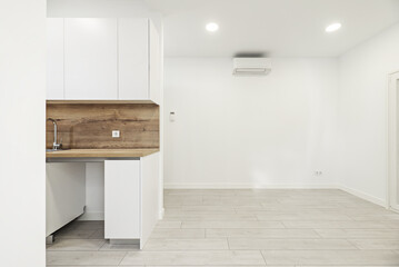 Image of a newly installed small kitchen with white furniture with backsplash and countertop of the same material in a loft-style apartment - obrazy, fototapety, plakaty