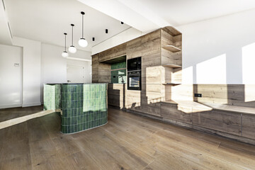 Large kitchen furnished with light oak wood furniture with a large island with a green marble countertop with tiles of the same color and globe lamps hanging from the ceiling