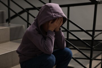 Child abuse. Upset boy sitting on stairs indoors