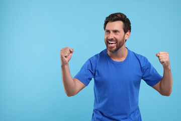 Emotional sports fan celebrating on light blue background, space for text