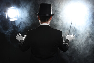 Magician with wand in smoke on stage, back view