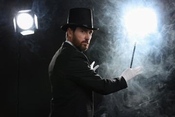 Magician wearing top hat and holding wand in smoke on stage