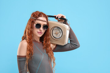 Stylish young hippie woman with retro radio receiver on light blue background