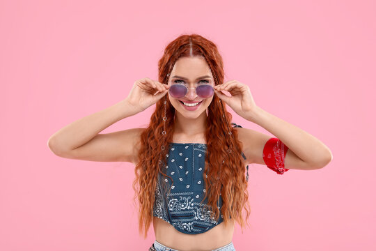 Stylish young hippie woman in sunglasses on pink background