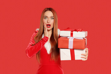 Fototapeta premium Emotional young woman with Christmas gifts on red background
