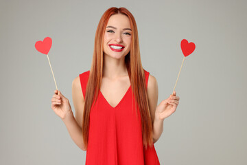 Young woman in red dress with paper hearts on light grey background