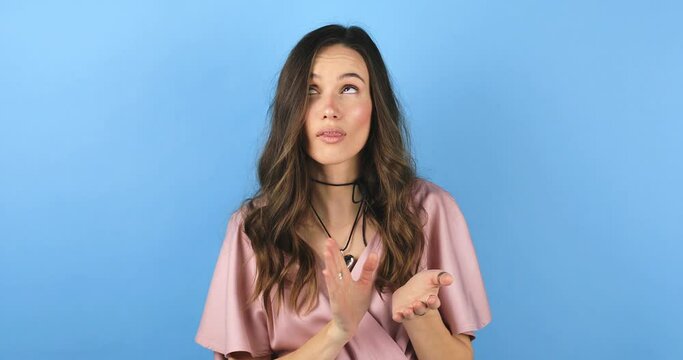 Pretentious brunette curly hair woman in pink dress clapping, and looking annoyed over blue background. Girl applauds with a grin, sarcasm sarcastically clapping her hands.