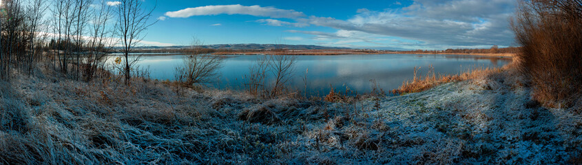 Panorama of the sunrise over the winter river. The sun rises over the lake. Autumn frost. The...