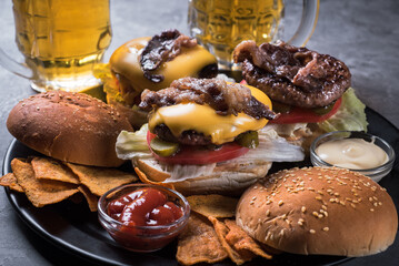 Beef burgers with beer on a black tray on a grey background.