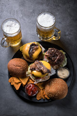 Beef burgers with beer on a black tray on a grey background.