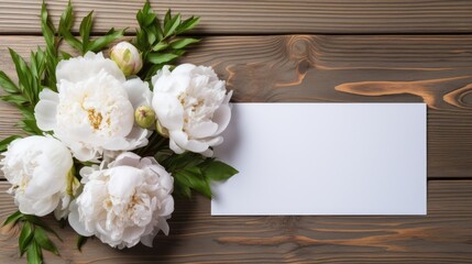 Bouquet of white peonies with empty blank of greeting card on wooden background. Top view mock up
