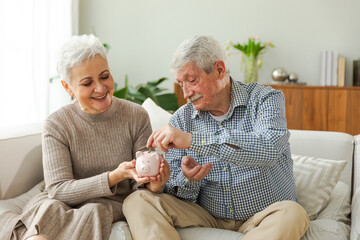 Saving money investment for future. Senior adult mature couple holding piggy bank putting money...