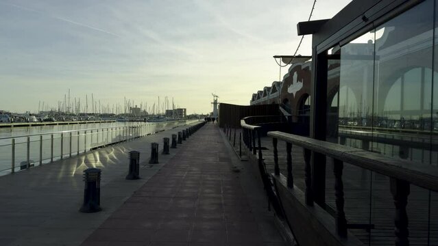 Walk in the port of Grao de Castellon in Spain in winter. Yachts and boats reflected in the water and glass of the display case. Walking along the boardwalk in the evening in December