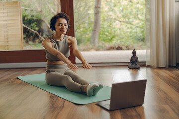 Active fit woman doing stretching exercise on mat in living room at home while use laptop