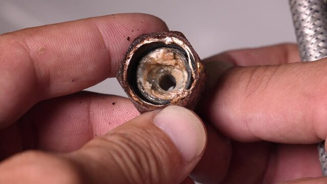 Plumber close-up holds used broken hose all rusty and on neck of flexible hose, full of plaque due to fact that there is lot of lime in water