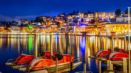 Fototapeta na wymiar Pedal boats on lake and city Lugano in blue hour - twilight