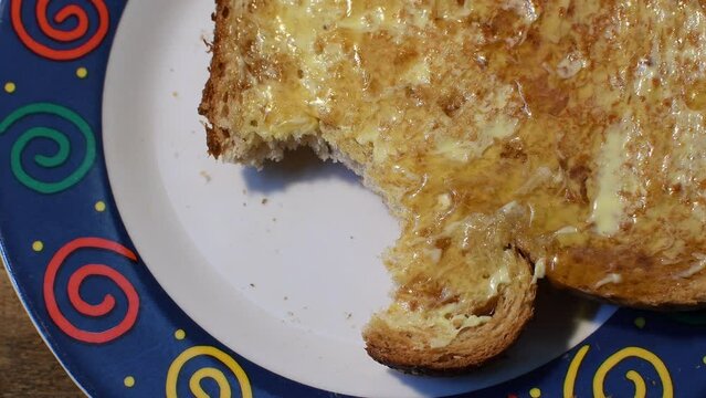Close-up looking down butter honey on sliced piece of Wholemeal toast bite taken out being returned to plate