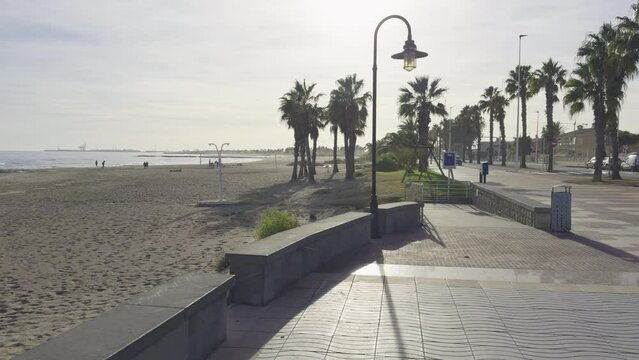 Vacationers on the beach of Spain among palm trees. Cyclists ride along the beach along the sea. Surfers on the waves in December. Grao, Castellon on the coast of Spain.