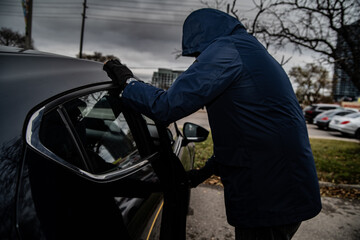 A car thief is breaking into a car in broad daylight in Toronto, Ontario, Canada.