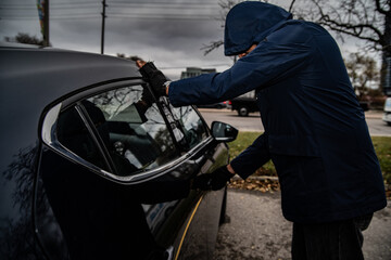 A car thief is breaking into a car in broad daylight in Toronto, Ontario, Canada. - obrazy, fototapety, plakaty