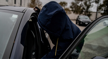 A car thief is breaking into a car in broad daylight in Toronto, Ontario, Canada.