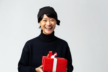 A cheerful Chinese woman holds a beautifully wrapped Christmas present, radiating happiness and beauty in festive celebration.