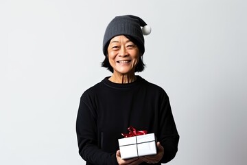 Mature Chinese woman in a festive Santa hat, holds a red Christmas gift, radiating joy.