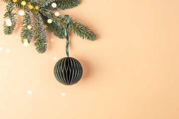Christmas bauble on fir branch with bokeh lights. New Year concept. Color of the year 2024 - Peach Fuzz background
