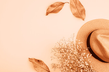 Female straw hat, autumn leaves and gypsophila bouquet on peach background. Top view, flat lay, copy space. Demonstrating color of the year 2024