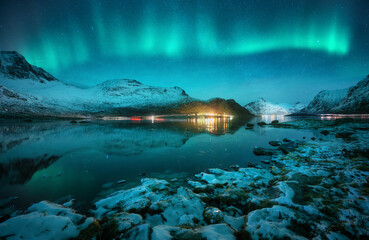 Aurora borealis over the snowy mountains, frozen sea, reflection in water at winter night in...