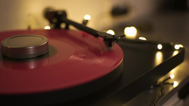 A vinyl record spins in the modern gramophone music player and plays an old disco. Close-up shot of custom vinyl turntable player with carbon tonearm. Pink vinyl record