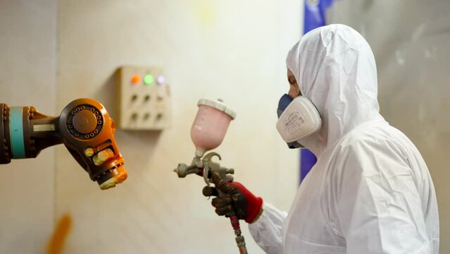 Employee painting a robot using a spray gun in a factory.