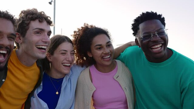 Joyful group of diverse student friends laughing together outside. Multi-ethnic teenage people having fun, bonding at city street. Friendship and youth concept.