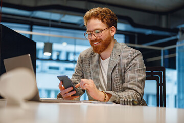 Handsome male boss holding phone while sitting in office during break time