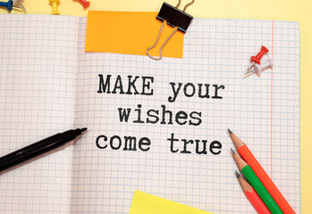 White notebook with inscription MAKE YOUR WISHES COME TRUE written in black pencil on a bright...