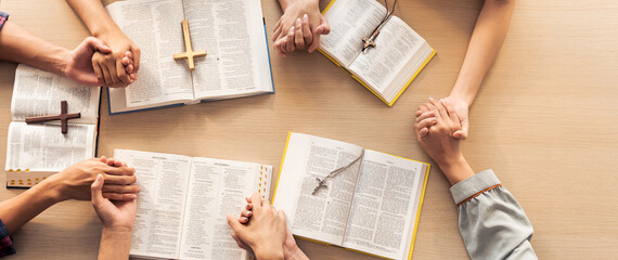 Cropped image of group of people praying together while holding hand on holy bible book at wooden church. Concept of hope, religion, faith, christianity and god blessing. Top view. Burgeoning. - obrazy, fototapety, plakaty