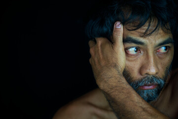 Dramatic portrait of homeless poor bearded man looking out aimlessly on black background, Concept...