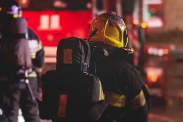 Foto op Canvas Group of fire men in protective uniform during fire fighting operation in the night city streets, firefighters brigade with the fire engine truck vehicle, emergency and rescue service © tsuguliev