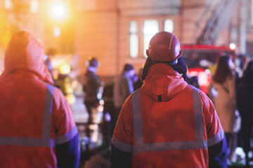 Group of fire men in protective uniform during fire fighting operation in the night city streets, firefighters brigade with the fire engine truck vehicle, emergency and rescue service