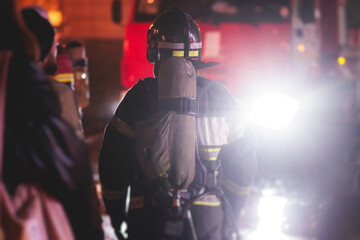 Group of fire men in protective uniform during fire fighting operation in the night city streets,...