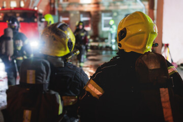 Group of fire men in protective uniform during fire fighting operation in the night city streets,...