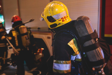 Group of fire men in protective uniform during fire fighting operation in the night city streets,...