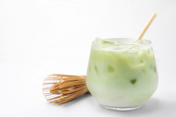 Glass of tasty iced matcha latte and bamboo whisk on white tiled table, closeup. Space for text