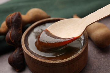 Taking tasty tamarind sauce with spoon from bowl on brown table, closeup - obrazy, fototapety, plakaty